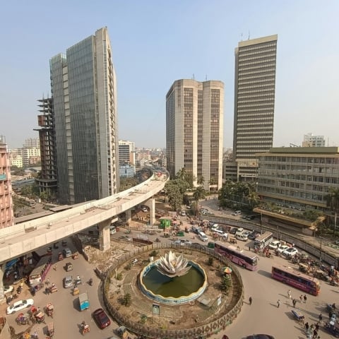 Aerial shot of an active financial district featuring high-rise towers, elevated roads, and central fountain plaza.